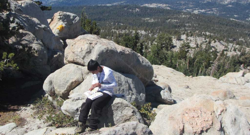 A person sitting on a rock at a high elevation journals. 